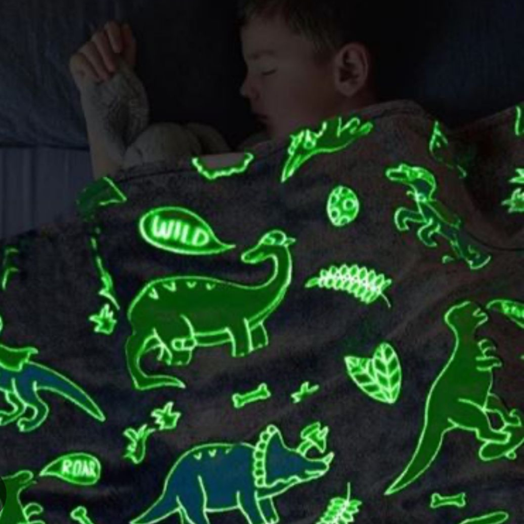 Decak pokriven svetlećim ćebetom koje sija u mraku sa motivima dinosaursa.