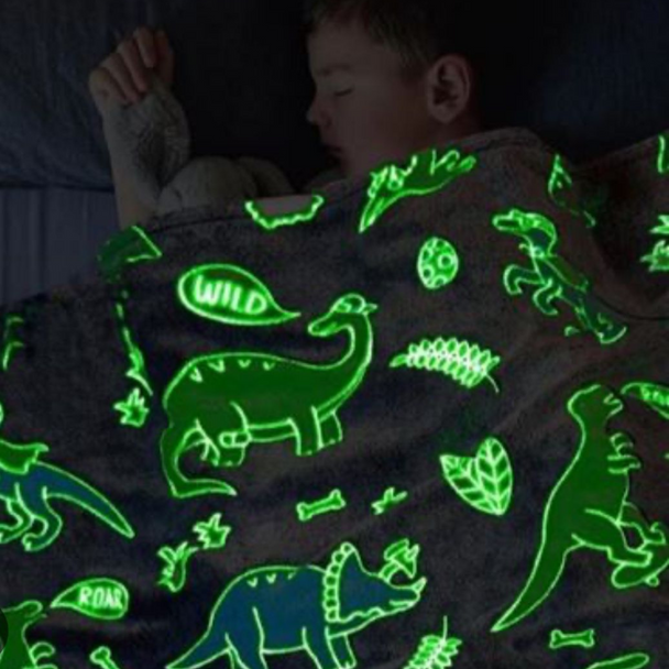 Decak pokriven svetlećim ćebetom koje sija u mraku sa motivima dinosaursa.